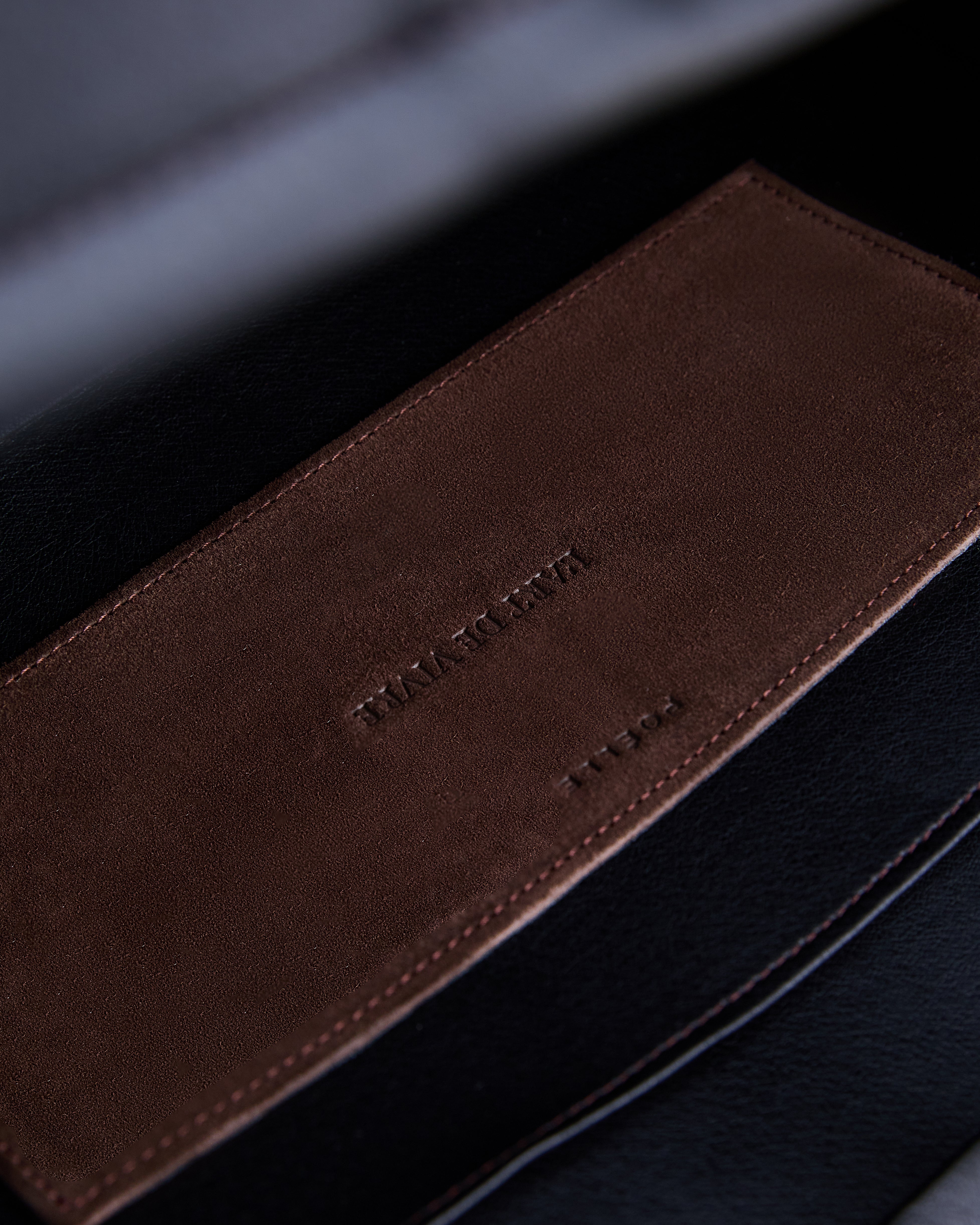 Close-up of Poelle Atelier luxury suede tote bag featuring brown suede detail with embossed branding