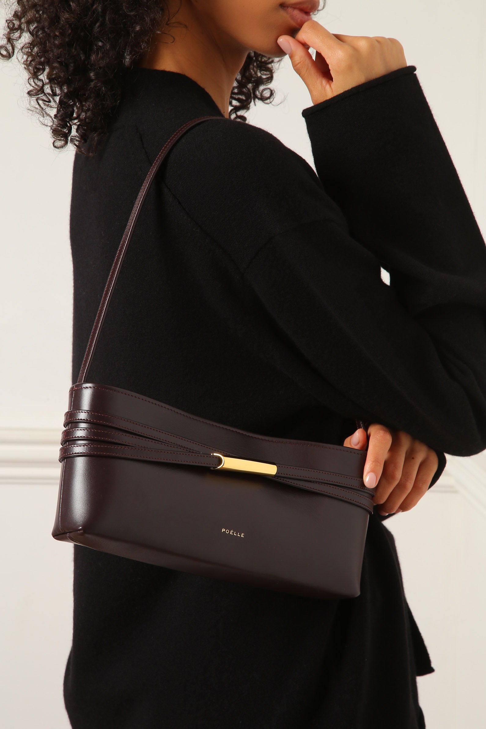 Poelle Atelier brown leather shoulder bag with gold accent worn by woman in black outfit