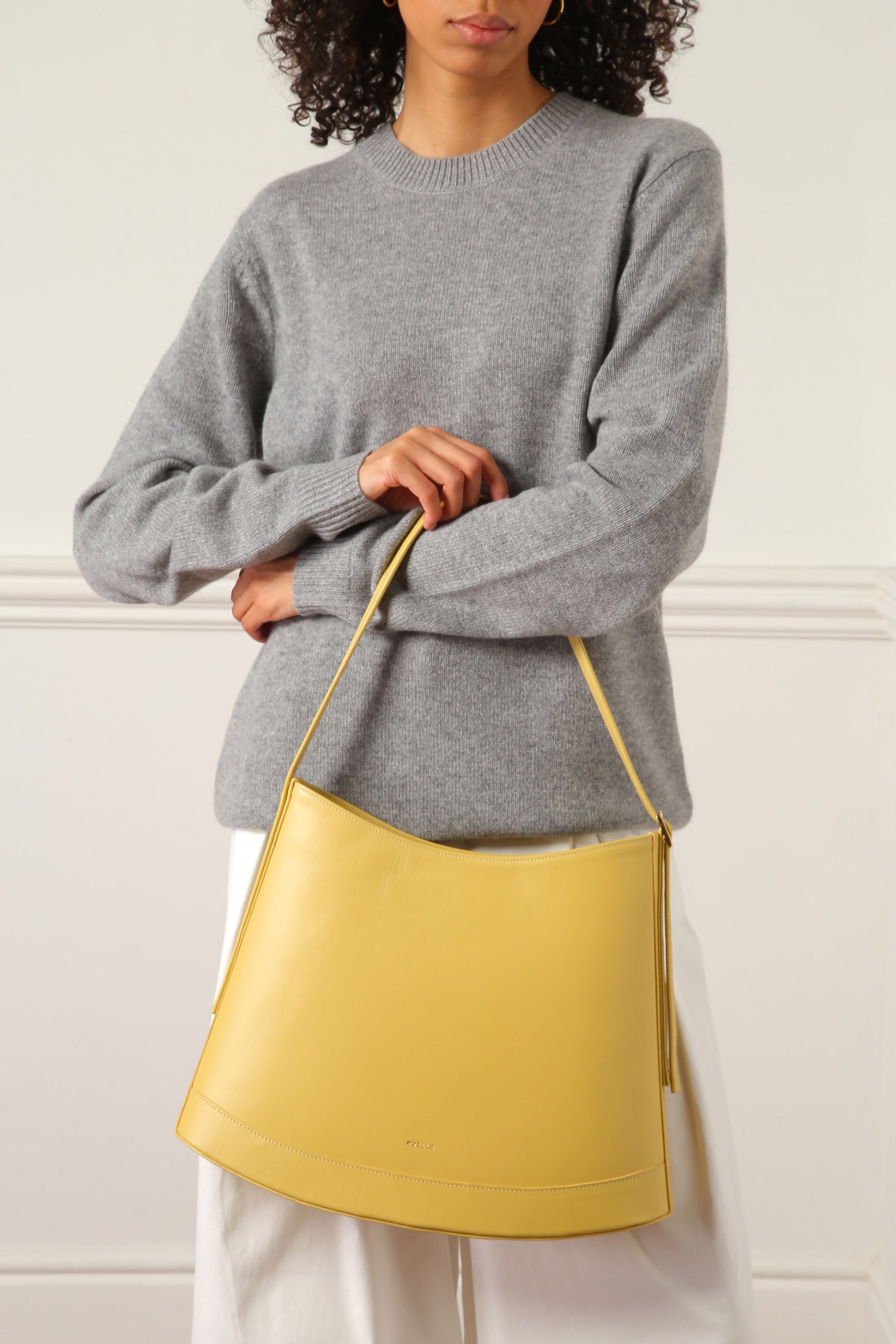 Yellow luxury minimalist sculptural bag by Poelle Atelier held by woman in gray sweater