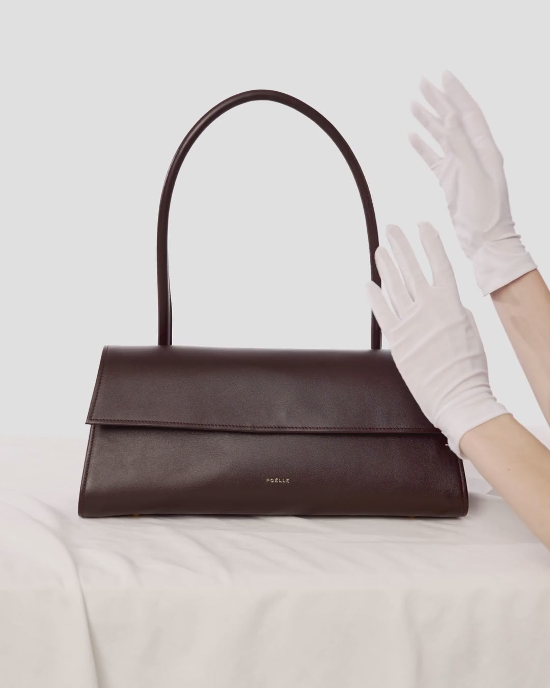 White gloves holding a Poelle bag